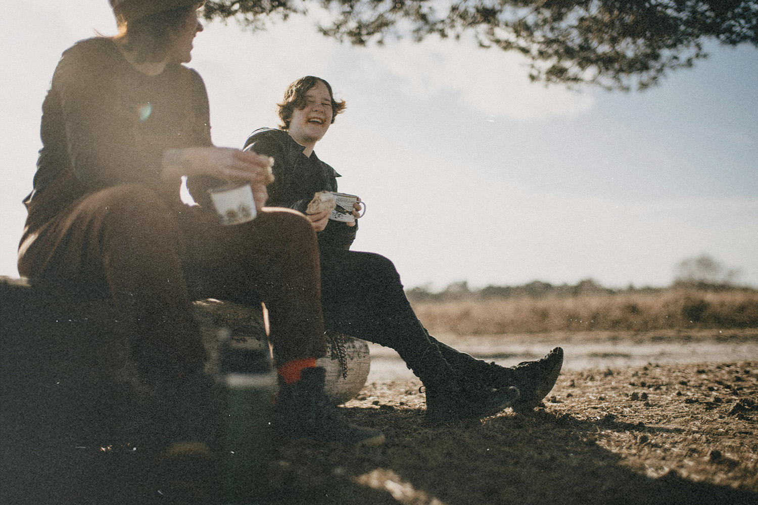 Two people sitting outdoors under a tree, enjoying coffee together as Miracles happen in quiet, natural surroundings.